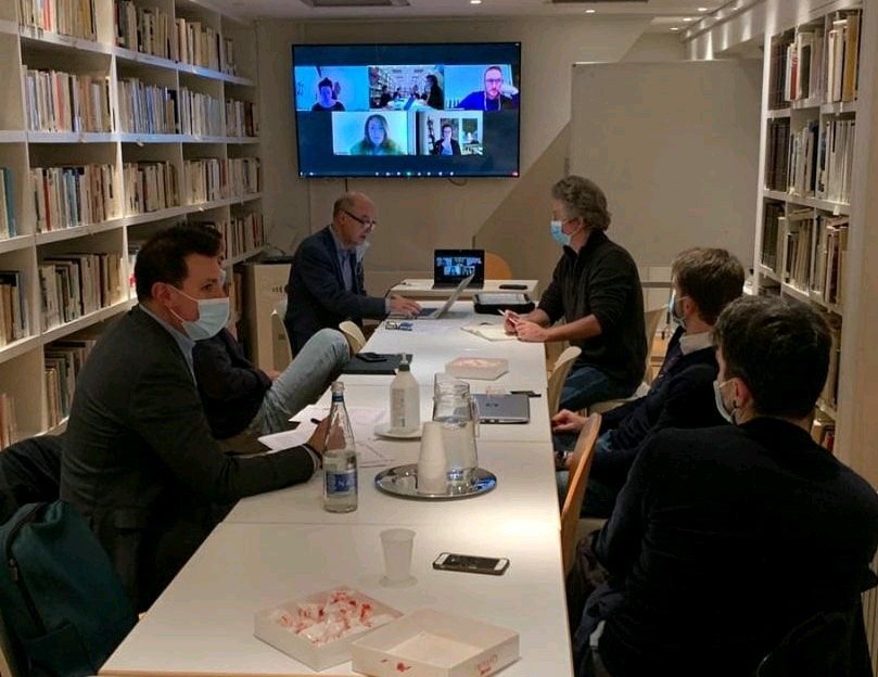 Participants around a table at the Italian Institute of Culture, with others connected by video